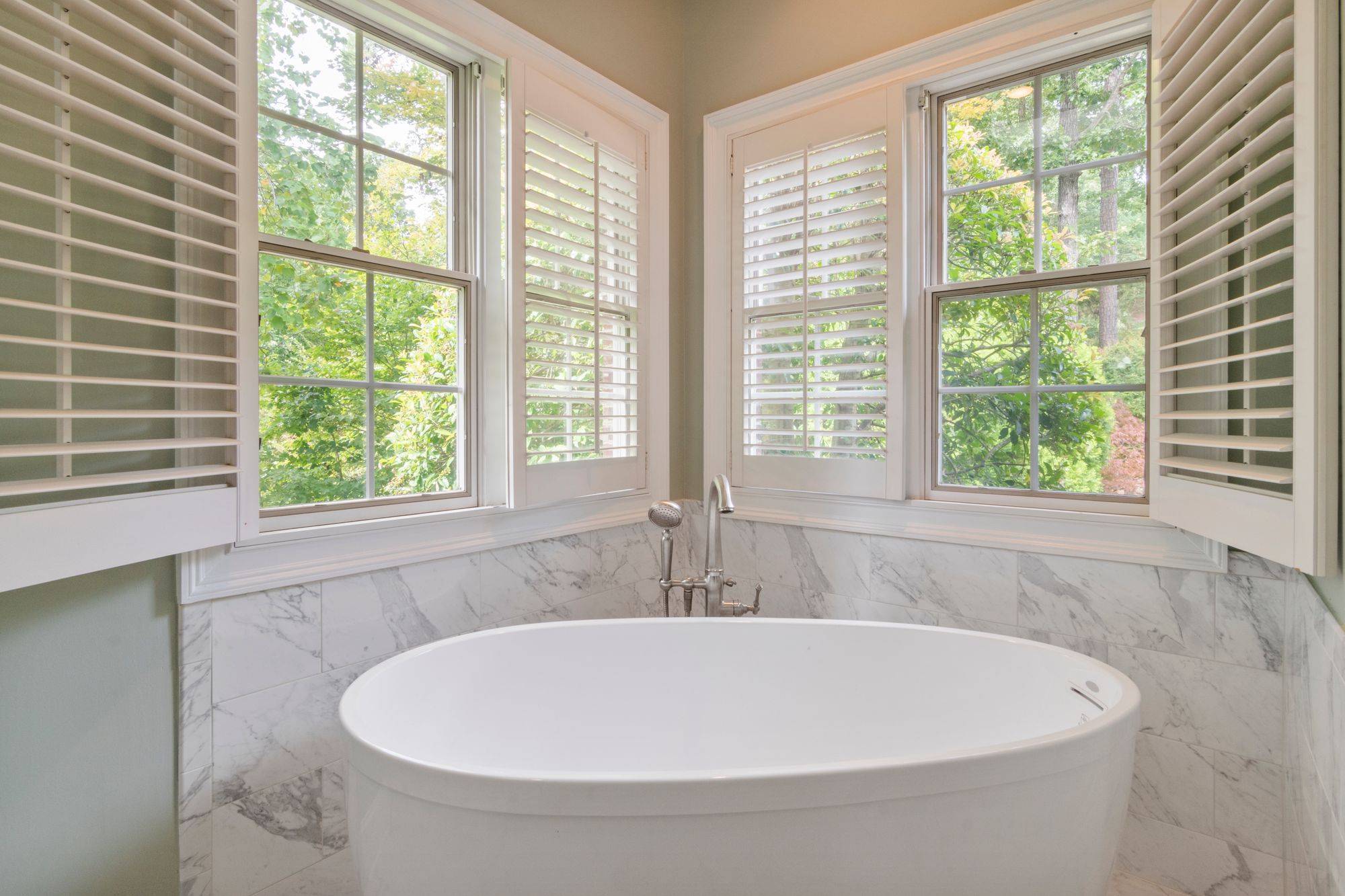 Marble bath with a freestanding tub beneath shuttered windows